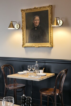 A dining area with a table set for two, two chairs, a framed portrait on the wall, and two wall-mounted lamps. - Les Hauts de Loire (Veuzain-sur-Loire)
