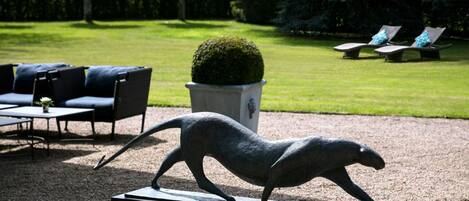 A sculpture of a wild cat on a pedestal in a garden with a lawn, seating area, and hedges.