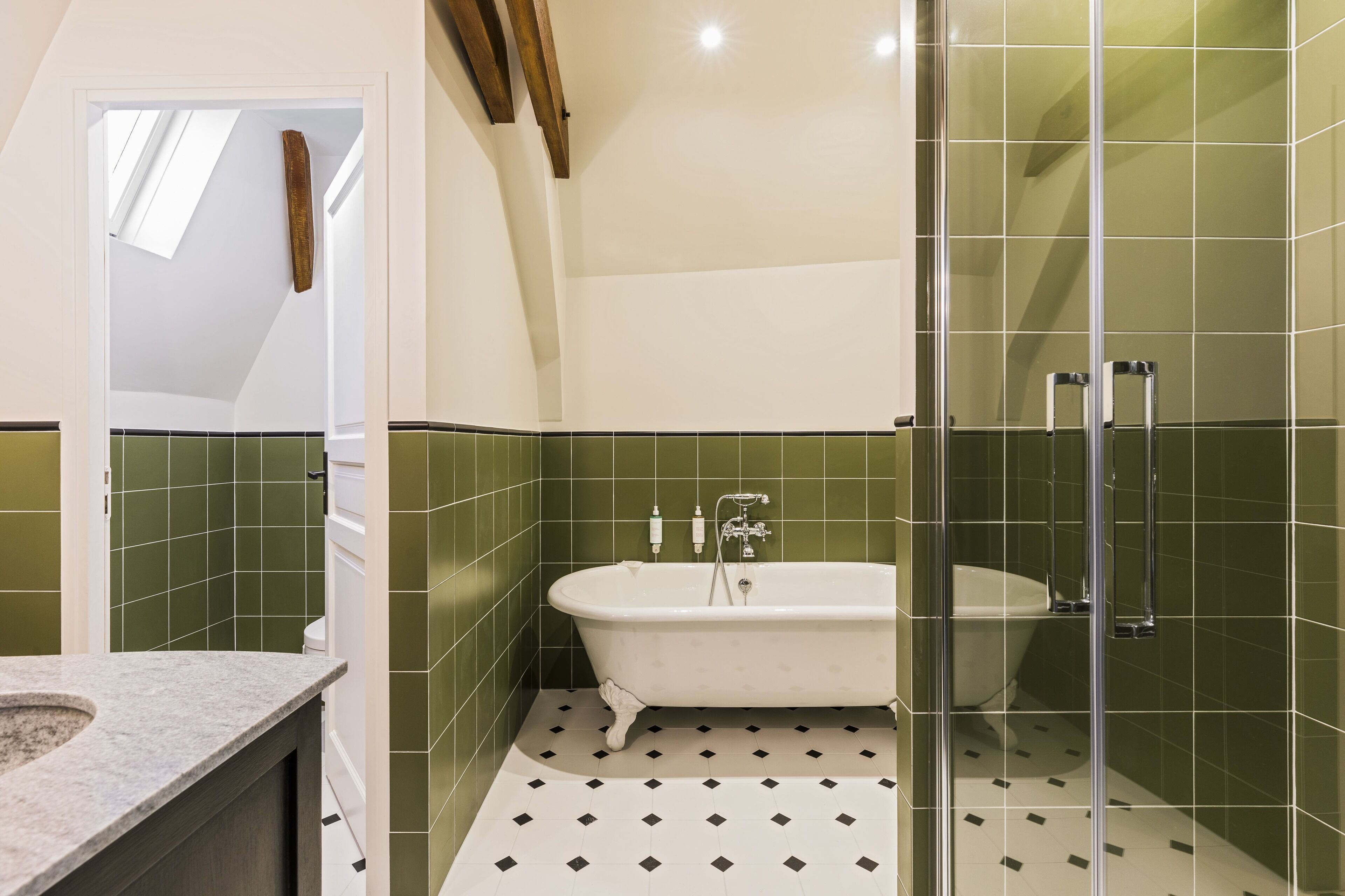 A bathroom with a freestanding bathtub, green tiled walls, and a patterned floor.