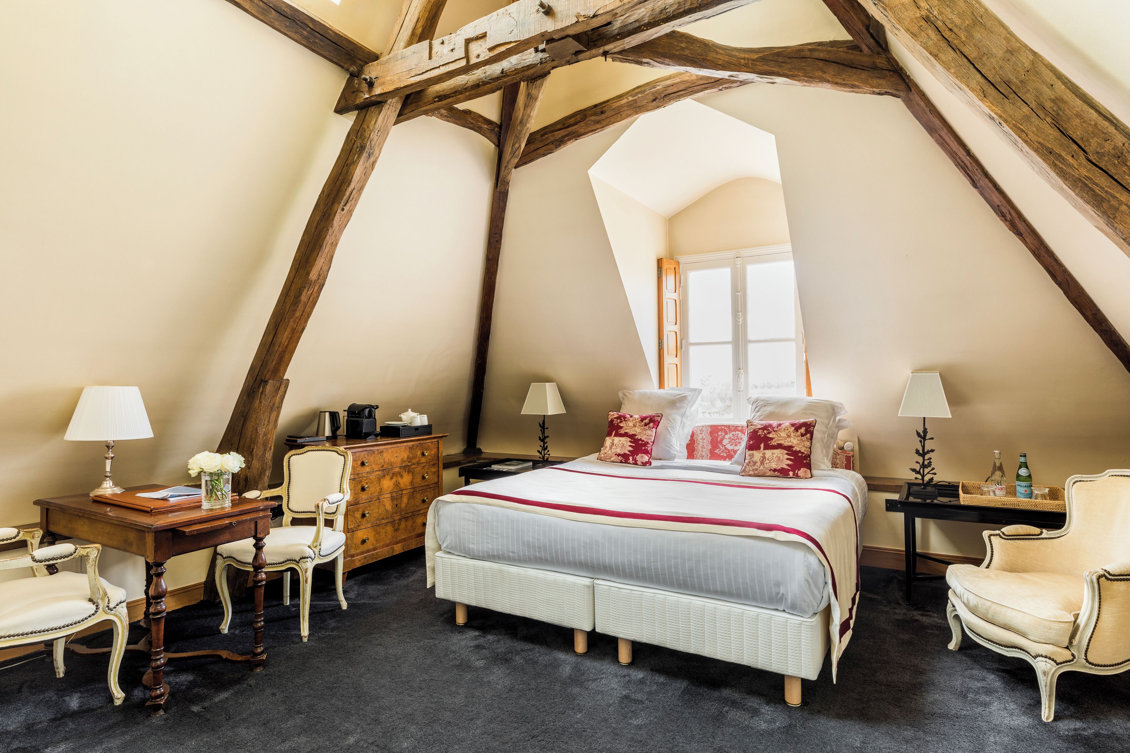 A bedroom with a large bed, two chairs, a dresser, and a desk.