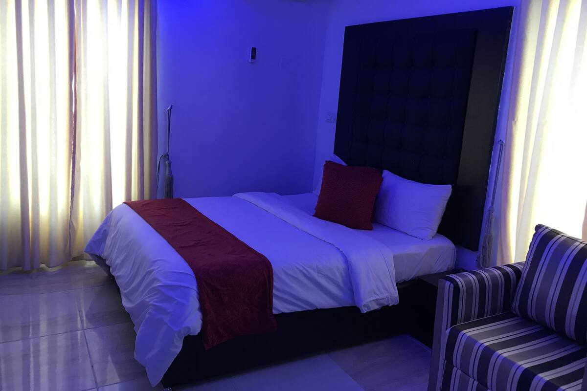A hotel room with a bed, a bedside table, a chair, and a window with curtains.