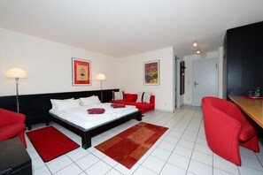 Quarto de hotel com cama, sofá vermelho, poltrona vermelha, escrivaninha e abajur.