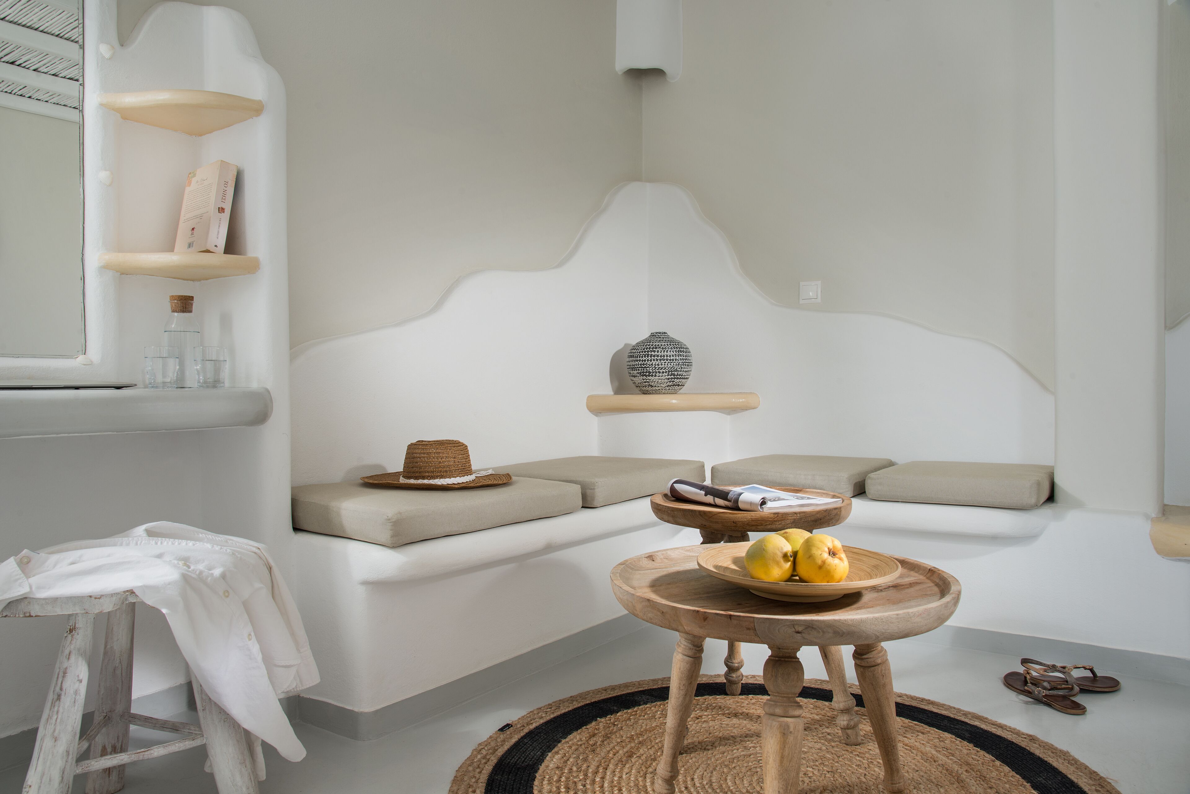 A minimalist room with a white sofa, a wooden table with lemons, a woven rug, and a window with a view.