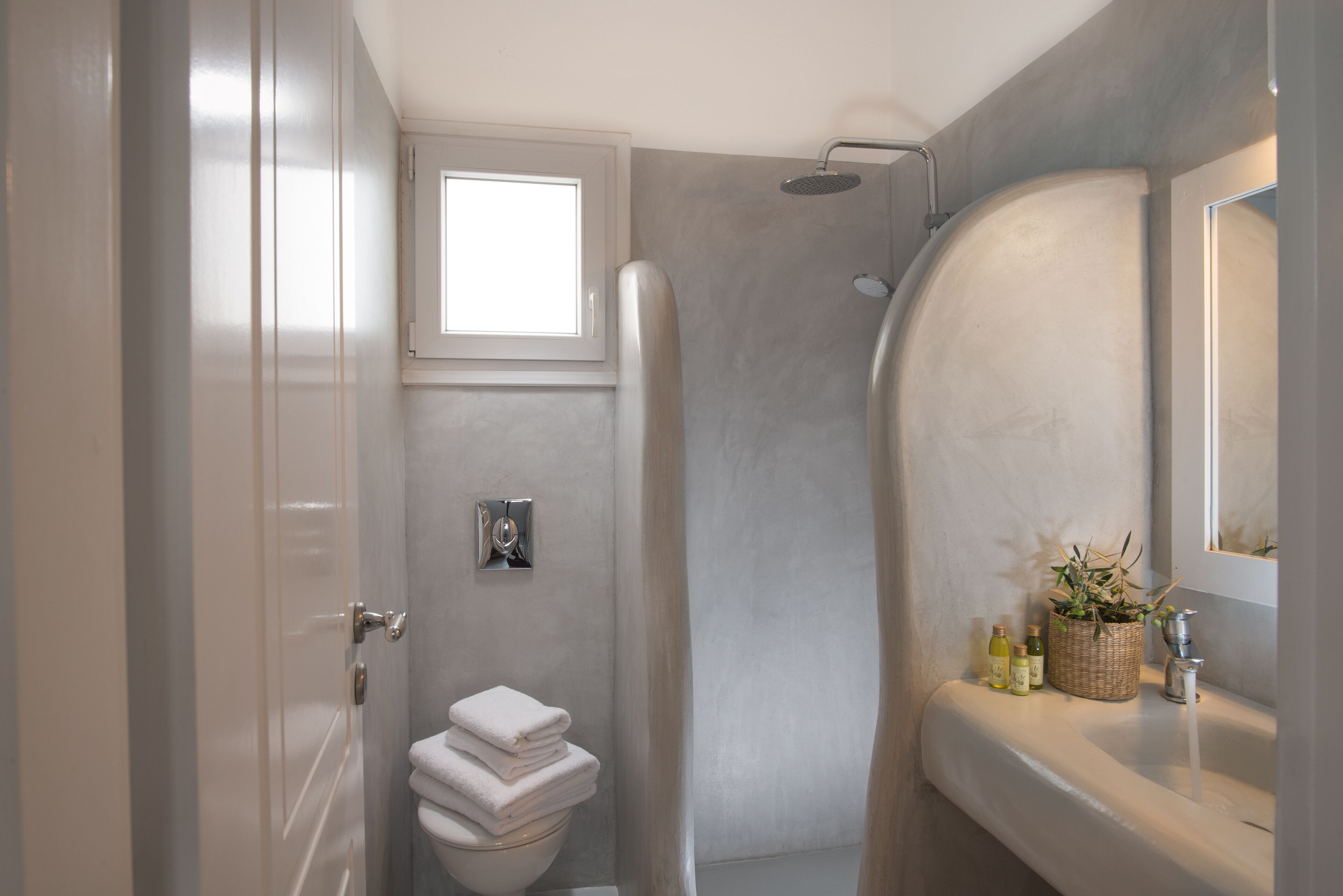 A bathroom with a shower, toilet, sink, and a small window.