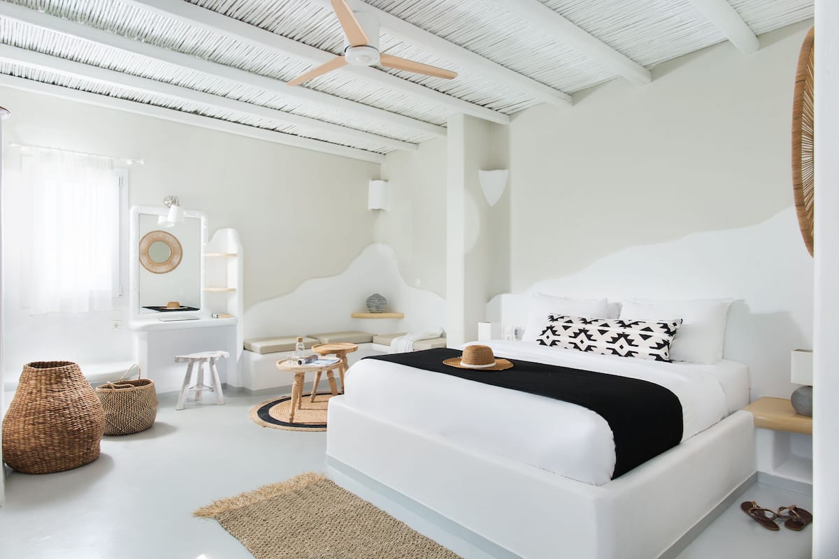 A modern bedroom with a white bed, a ceiling fan, and a large window with curtains.