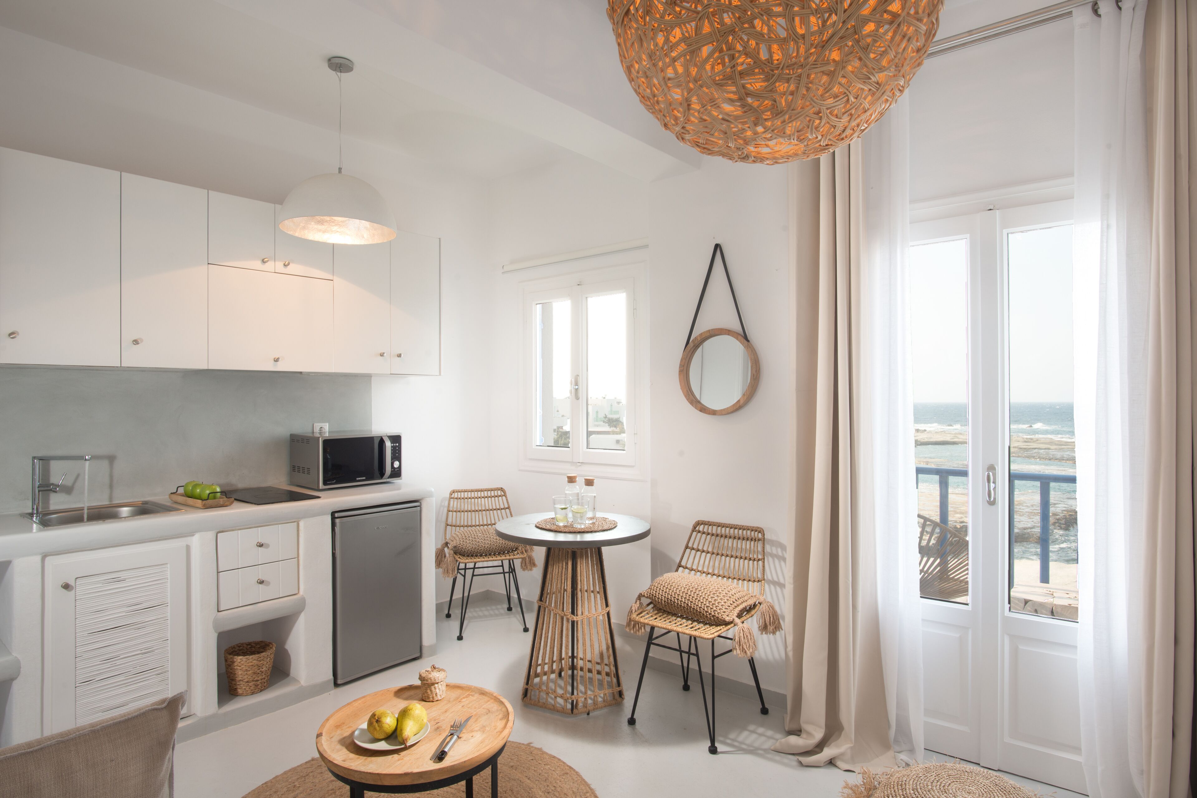 A modern kitchen with white cabinets, a microwave, and a dining area with wicker chairs and a round table.