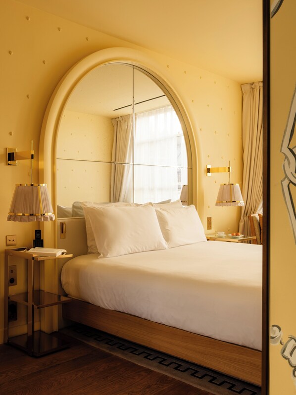 Una habitación de hotel con una cama grande, una mesita de noche, una lámpara y un espejo.