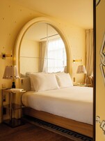 A hotel room with a large bed, a bedside table, a lamp, and a mirror.