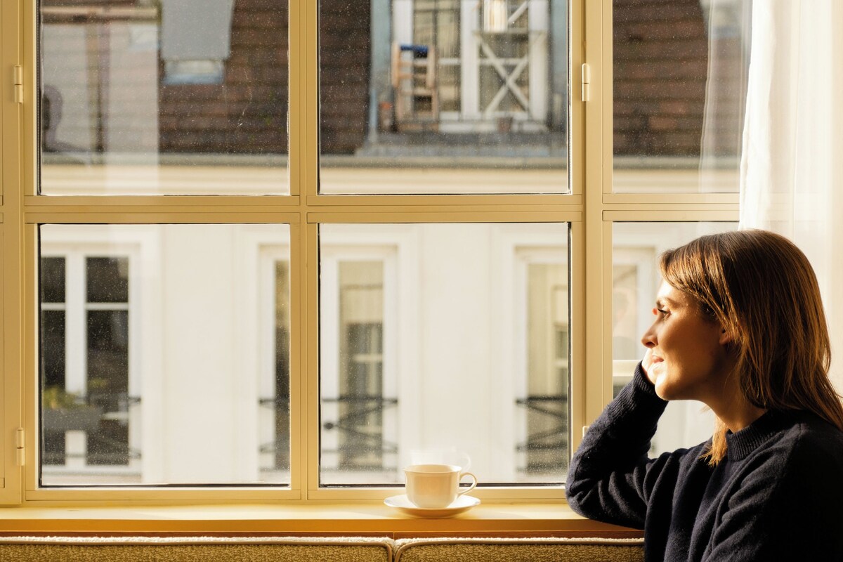 Una persona sentada en un sofá cerca de una ventana, con una taza en el alféizar.