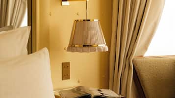 Habitación de hotel con cama, mesita de noche con lámpara, una silla y ventana con cortinas.