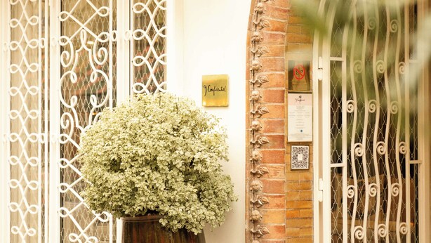 A building facade with ornate metal gates, a potted plant, and a sign. - 9Confidentiel (Paris)