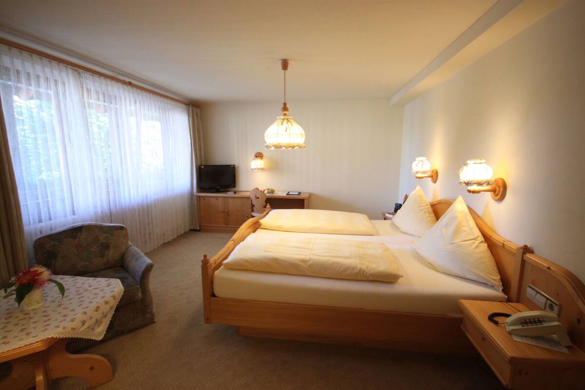 Habitación de hotel con cama doble, un escritorio pequeño con lámpara, televisor y una silla.