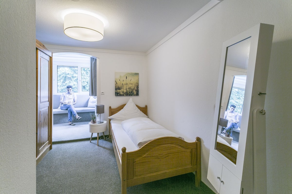 Un dormitorio con cama de madera, una mesita de noche, un espejo y una ventana.