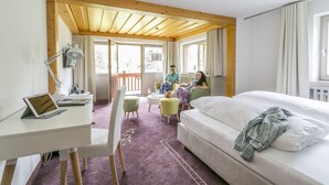 A hotel room with a bed, a desk with a laptop, a chair, a small table, and a balcony with a view of the outdoors. - Hotel Imbery (Hinterzarten)