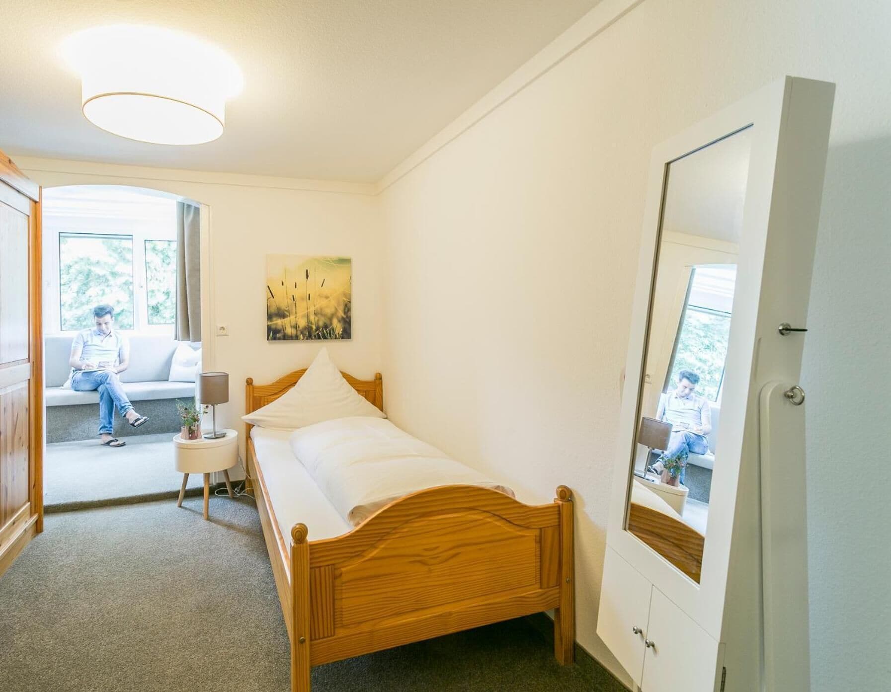 Un dormitorio con cama de madera, una mesita de noche, una lámpara, una ventana con vistas y una puerta.