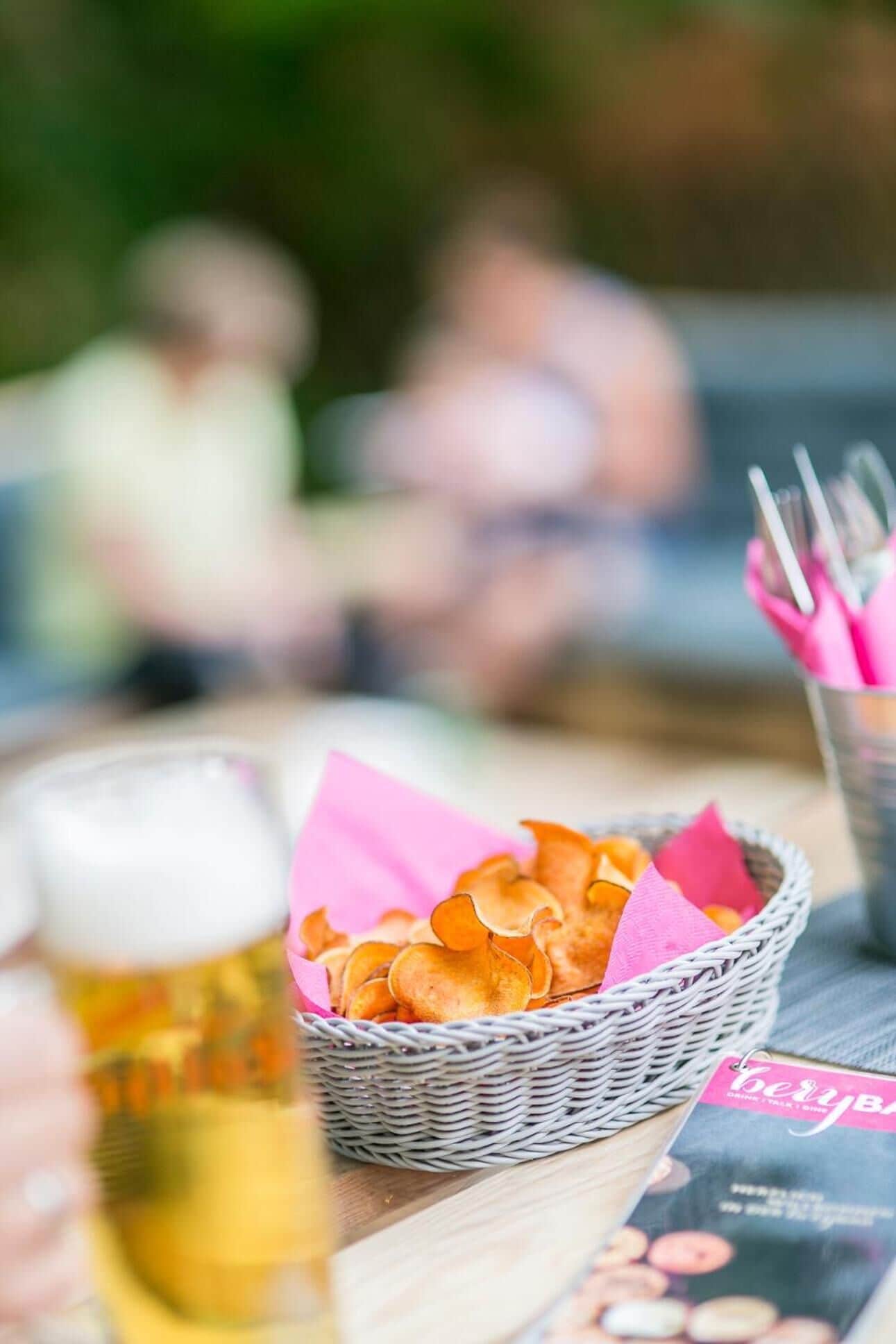 A wicker basket filled with snacks on a table with a beer glass and a menu.