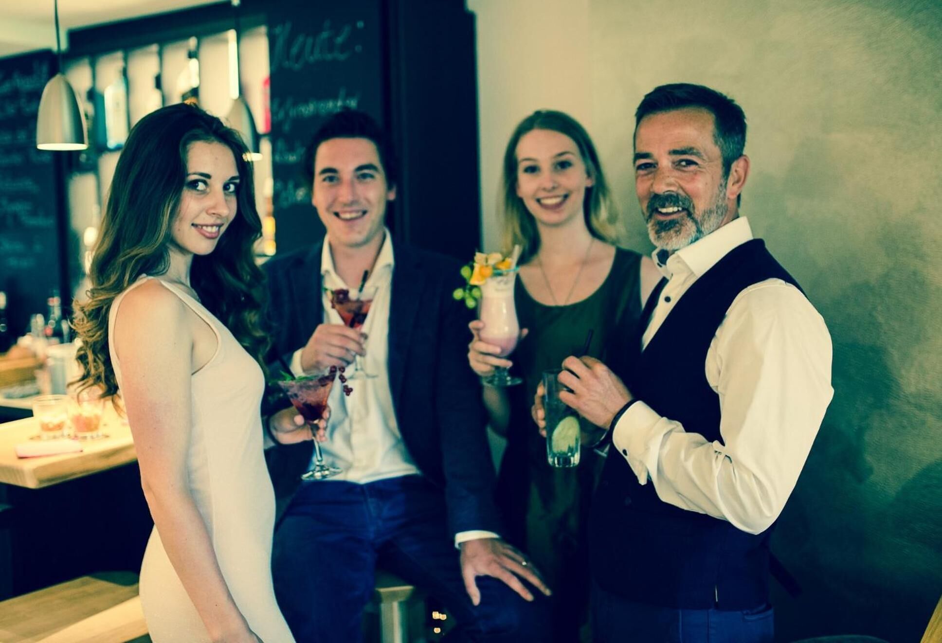 Un groupe de personnes se trouve dans un bar, avec un comptoir et des lampes suspendues.