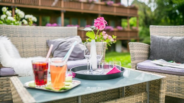 A wicker sofa with cushions, a tray with drinks and glasses, and a vase with flowers. - Hotel Imbery (Hinterzarten)