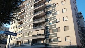 Un edificio residencial de varios pisos con balcones, entrada de garaje y zona de estacionamiento.