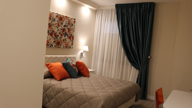 Una habitación de hotel con cama, una mesita de noche con lámpara, una pequeña mesa y una ventana con cortinas.