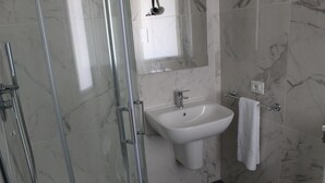 Un baño moderno con cabina de ducha de vidrio, un lavabo blanco y pared cubierta de mármol.