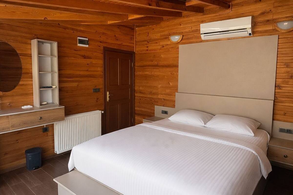 Une pièce aux murs lambrés, comprenant un lit, une commode, un radiateur et un climatiseur fixé au mur.