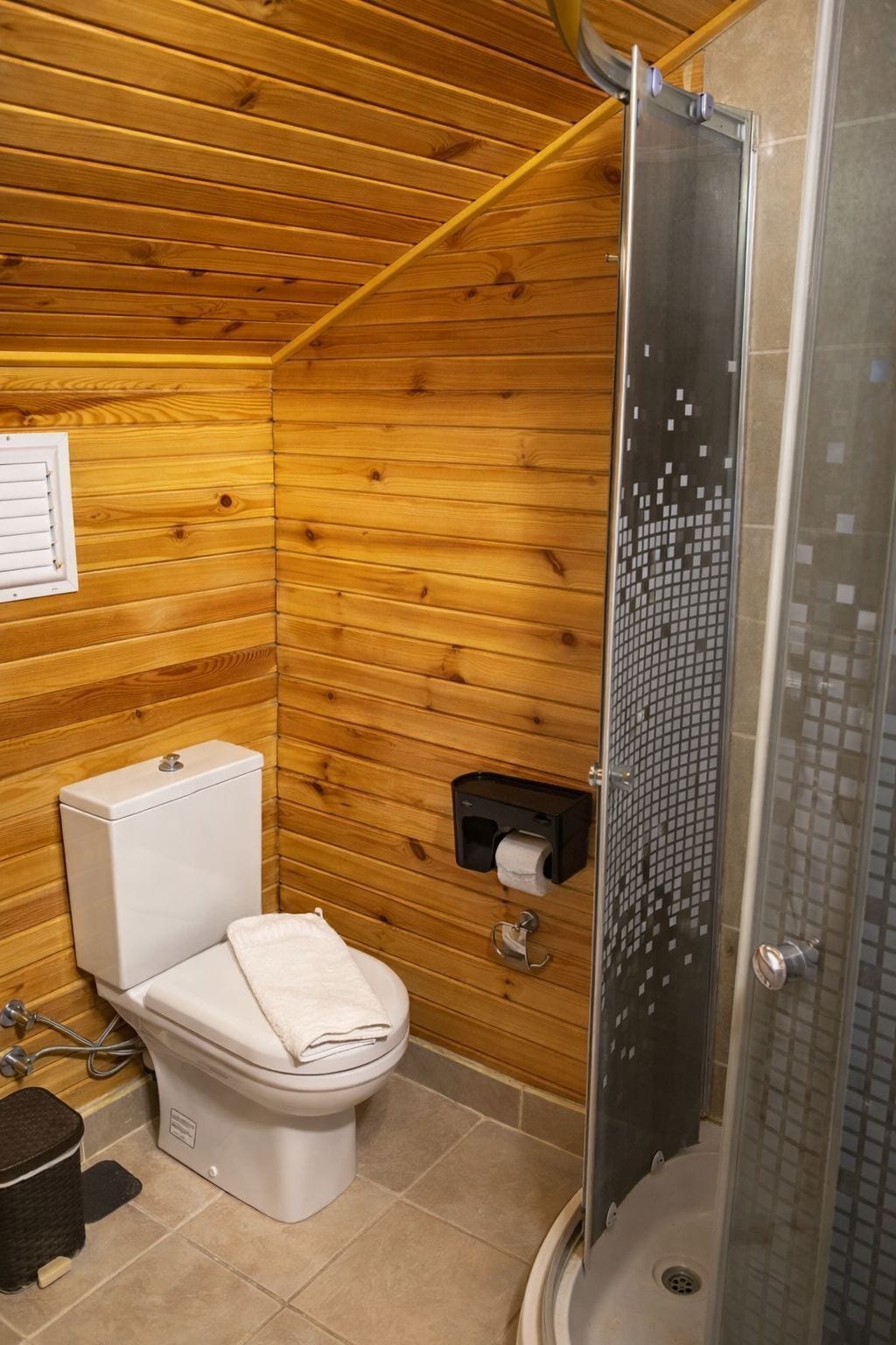 Casa de banho com painéis de madeira, com sanita, chuveiro e porta-papel higiénico.