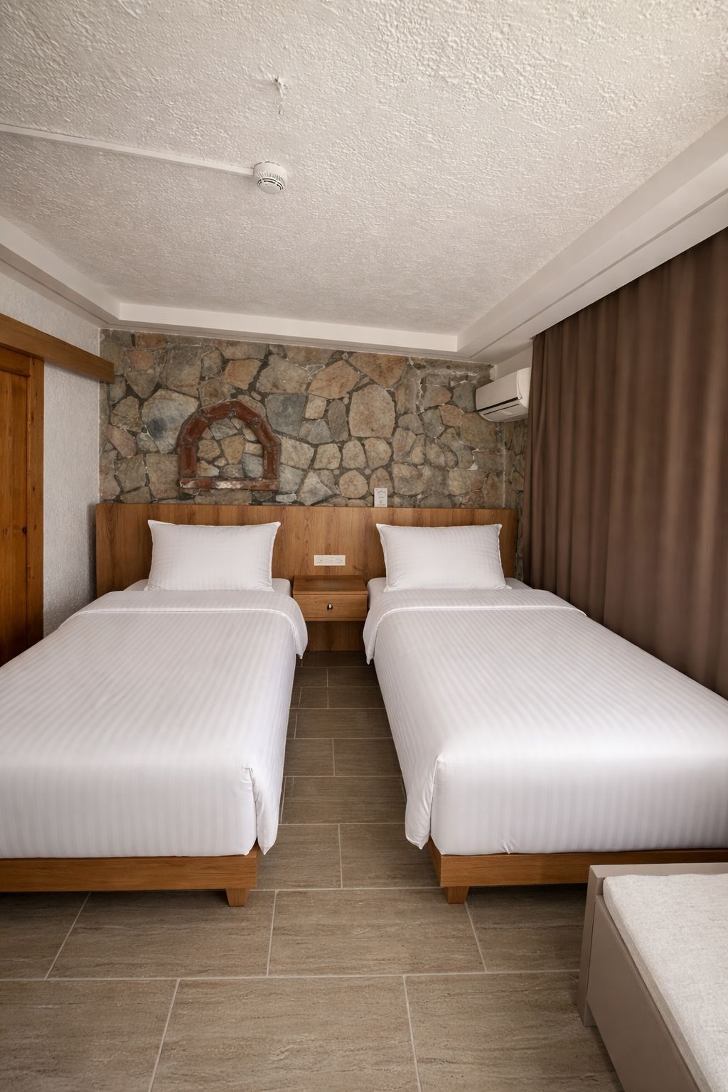 A hotel room with two beds, a stone wall, and a wooden headboard.