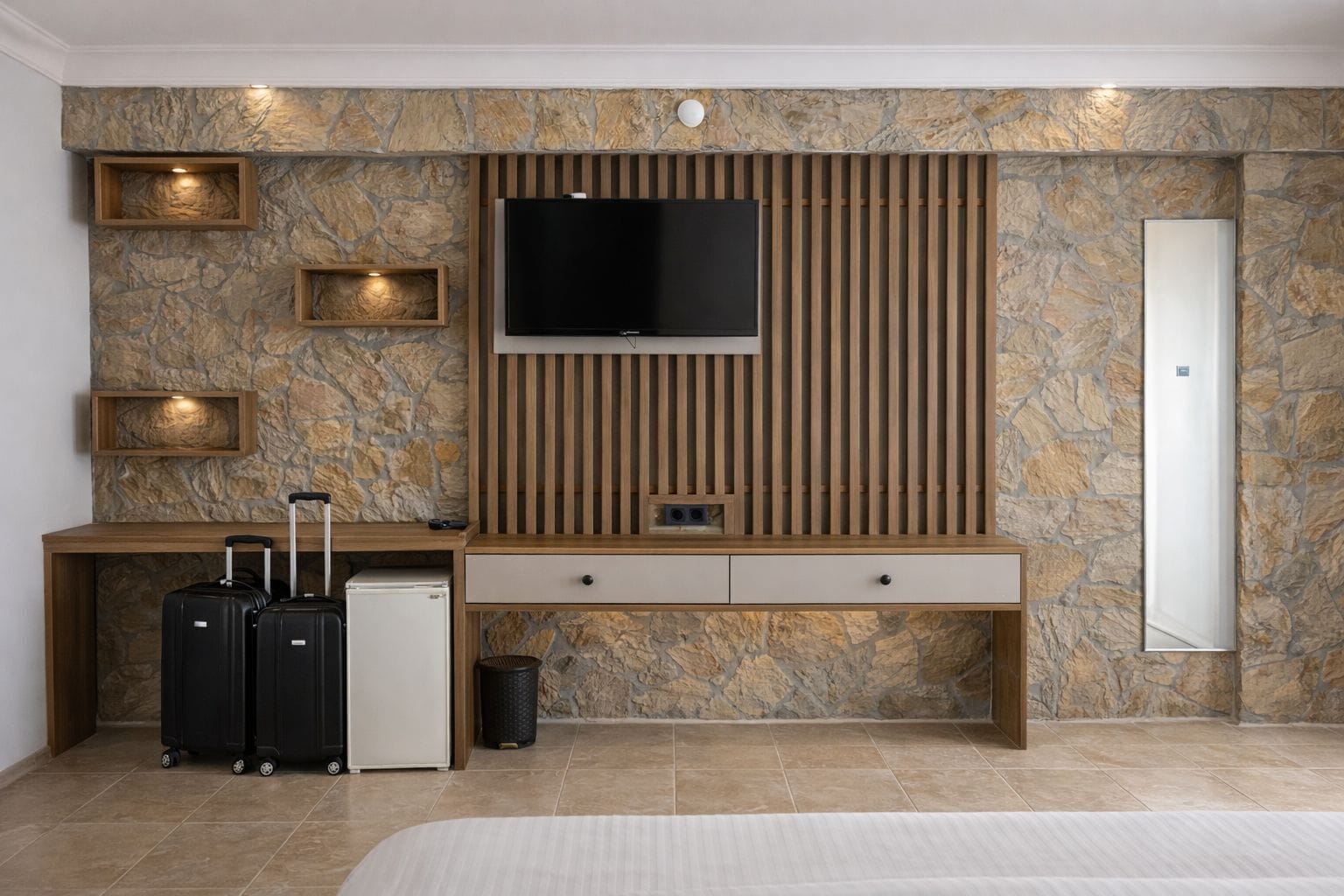 Une chambre d’hôtel avec un mur en pierre, un téléviseur fixé sur un panneau en bois, un bureau avec un miroir et un lit.