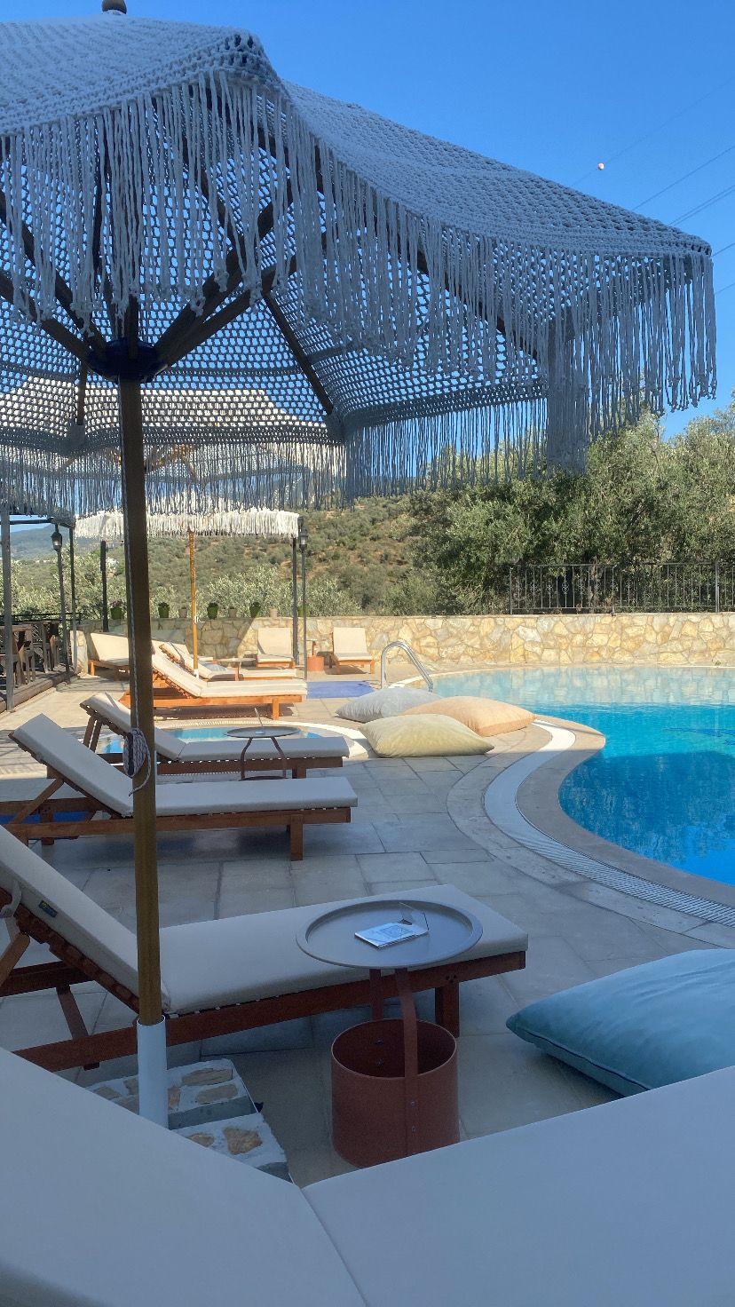 Zona de piscina con sillones de descanso, un muro de piedra y una sombrilla grande.