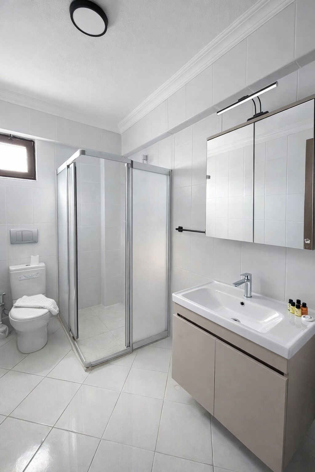 Uma casa de banho moderna com cabine de duche em vidro, sanita, lavatório com espelho e armário.