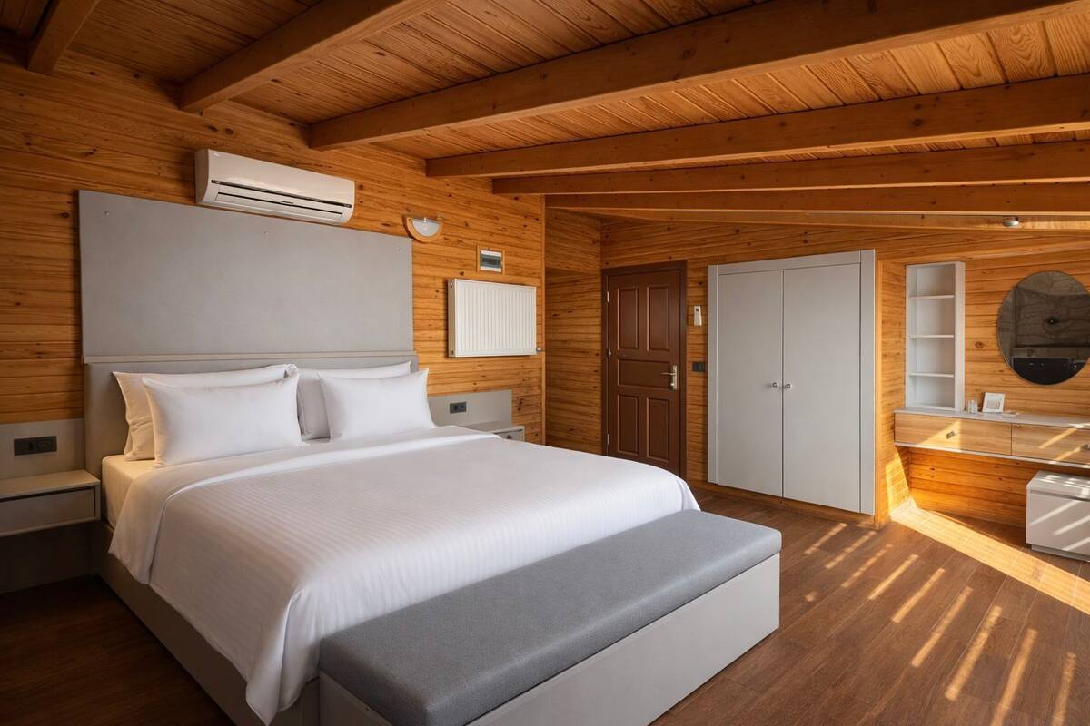 Une chambre à coucher aux murs lambrissés, comprenant un lit, des tables de chevet, une armoire et un miroir.