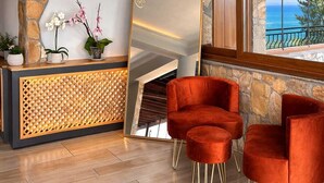 Un espace d’accueil avec un mur en pierre, un comptoir de réception en bois et deux fauteuils en velours rouge.