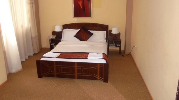 A hotel room with a large bed, a nightstand, a lamp, and a painting on the wall. - Pacific Hotel (Addis Ababa)