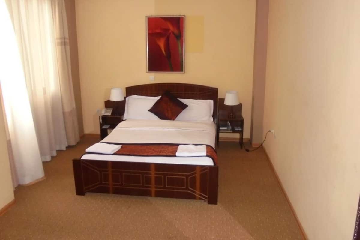 A hotel room with a large bed, a nightstand, a lamp, and a painting on the wall.