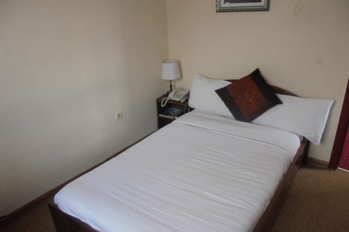 A neatly made bed with white linens, a bedside table with a lamp, and a framed picture on the wall.