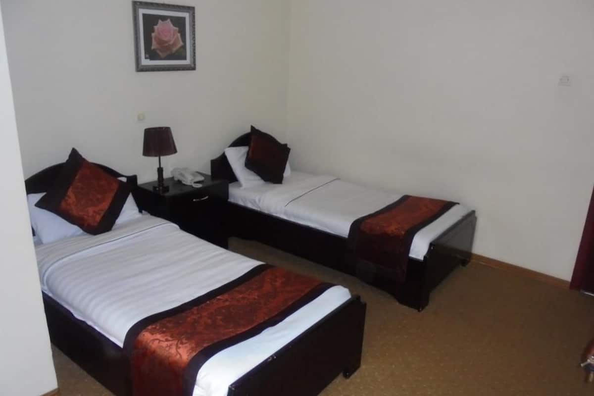 A hotel room with two beds, each with a red and black bedspread, a bedside table with a lamp, and a framed picture on the wall.