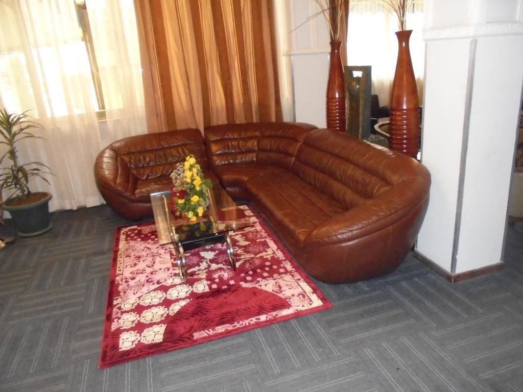 Una sala de estar con un sofá de cuero marrón, un tapete rojo con estampado y un jarrón con flores amarillas.