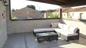 An outdoor patio with a sectional sofa and two side tables, a tiled floor, and a brick wall.