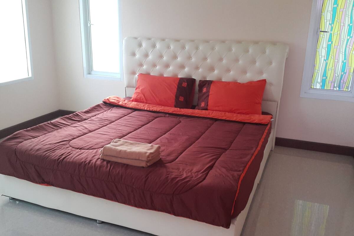 Un lit bien fait, recouvert d’une couvre-lit rouge et blanche, avec une tête de lit blanche à motifs et deux oreillers rouges.