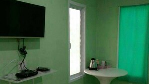 A small room with green walls, a flat-screen TV mounted on the wall, a small table with a kettle, and a window with a green curtain. - Yamsurl House Resort (Nikhom Phatthana)