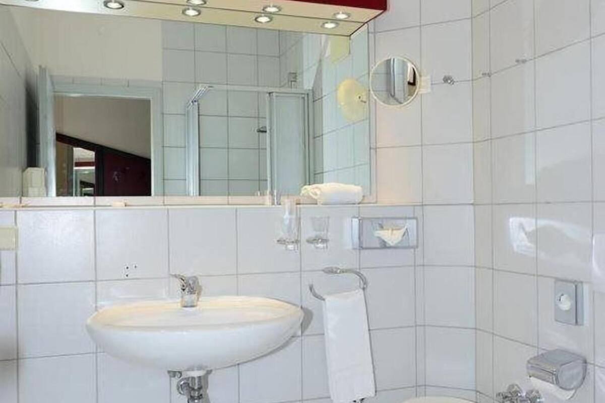 A bathroom with a white sink, toilet, and bidet. There is a mirror above the sink and a towel rack.