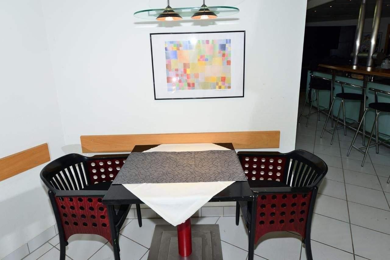 Uma área de refeições com mesa e cadeiras, uma obra de arte emoldurada na parede e um bar ao fundo.