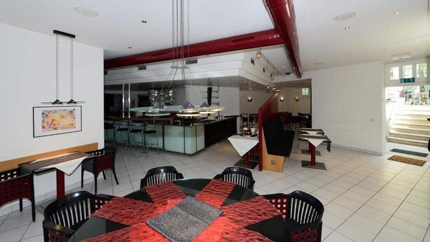 A modern dining area with a central island, black and red patterned tablecloths, and a kitchen in the background. - Art Hotel Weimar (Weimar)