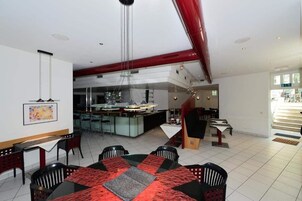 Un comedor moderno con una isla central, manteles estampados en negro y rojo, y una cocina al fondo.