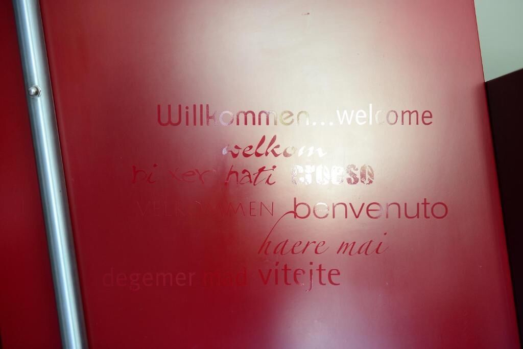 A red wall with multilingual welcome messages in various languages.