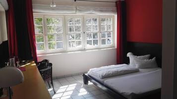 Un dormitorio con cama, escritorio con lámpara y ventana con cortinas.