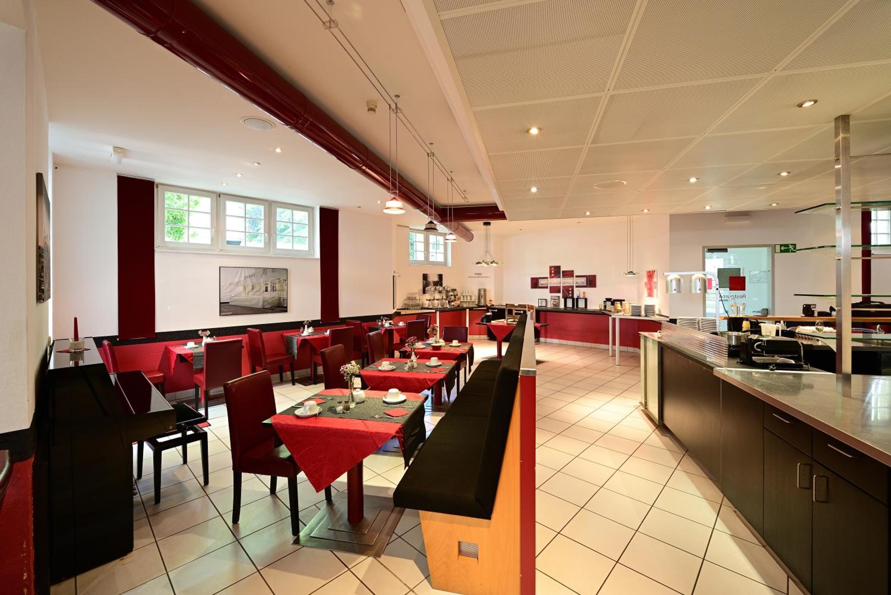 A spacious restaurant with high ceilings, red and black seating, and a long counter.