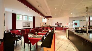 A spacious restaurant with high ceilings, red and black seating, and a long counter.