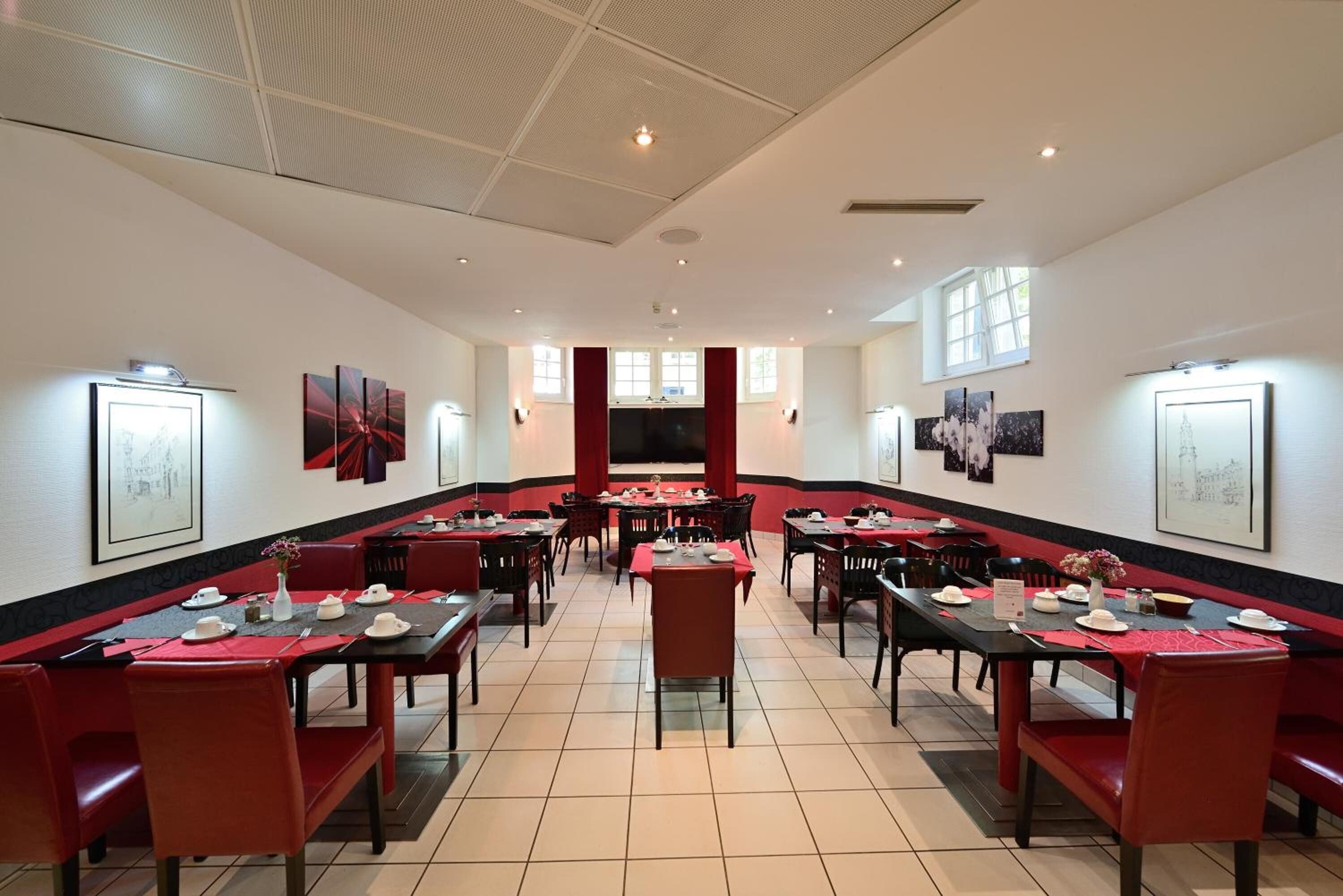 A spacious dining area with multiple tables and chairs, red accents, and framed artwork on the walls.